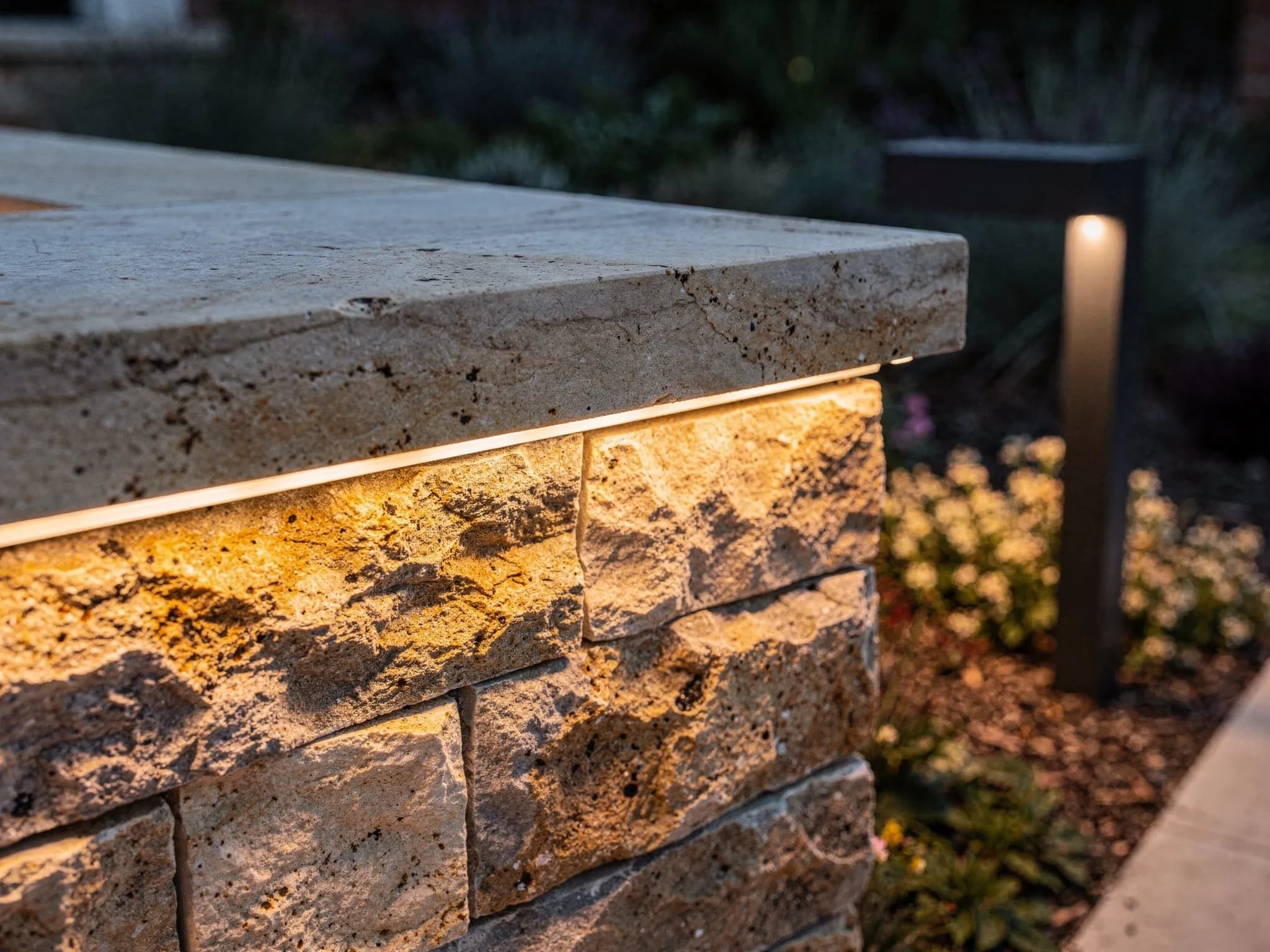 Under-cap lighting washes a sandstone sitting wall in gentle, glare-free warmth — comfortable for guests, beautiful from the house.